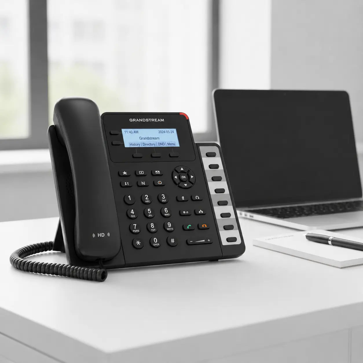 Grandstream GXP1628 Gigabit IP phone placed on a modern office desk alongside a laptop, ideal for business VoIP communication and office productivity.